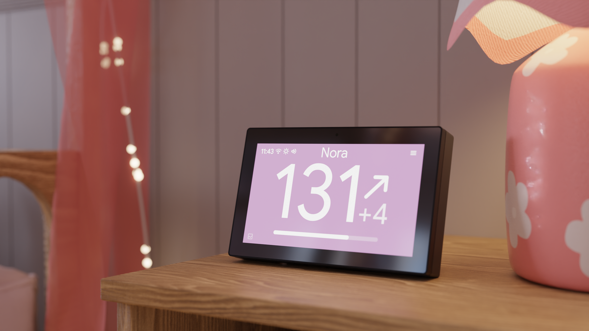 sugardash on a bedside table beside a pink lamp, displaying glucose in mg/dL