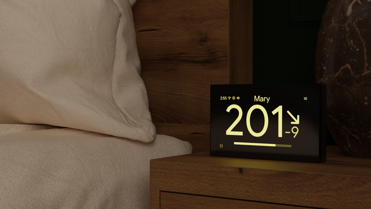 sugardash on a wooden nightstand beside a bed, displaying glucose in mg/dL with a yellow nighttime screen